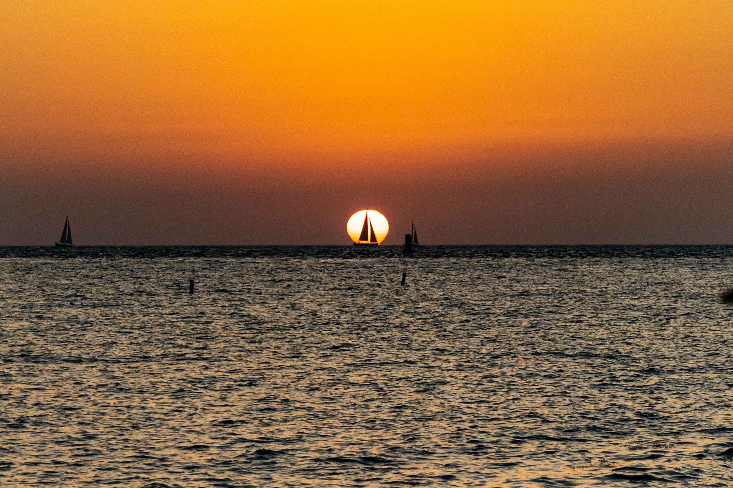 The sun sets over the ocean silhouetting a sailboat on the horizon in the Florida Keys.